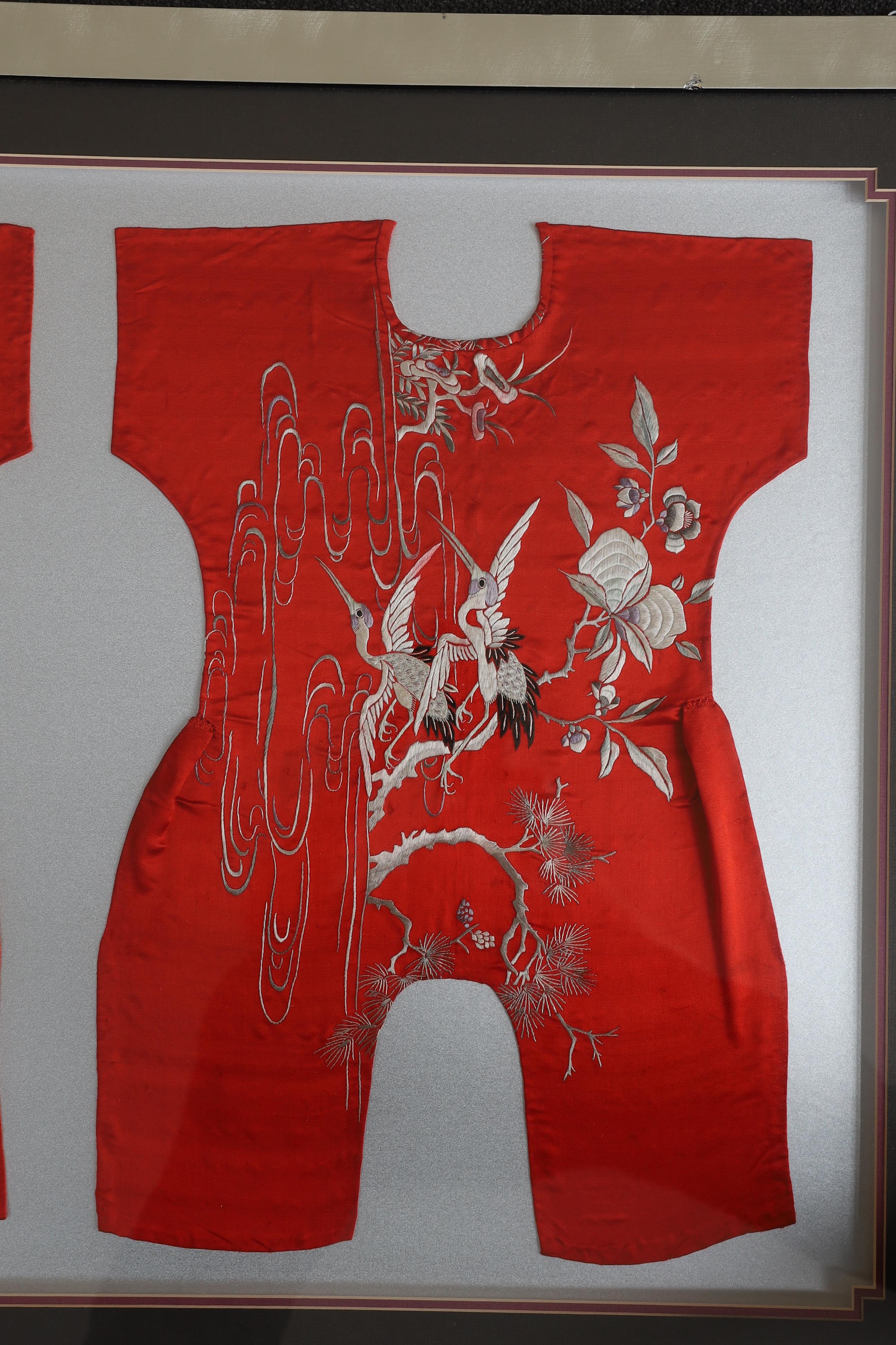 Three early 20th century Chinese framed embroideries: two purple baby’s bibs embroidered with multi-coloured silk threads, and another red silk child’s “romper suit”, embroidered with white and pastel embroidery, mounted